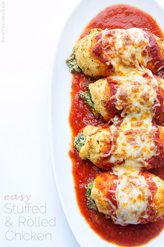 Four stuffed chicken rolls on a plate topped with marinara and mozzarella cheese. 