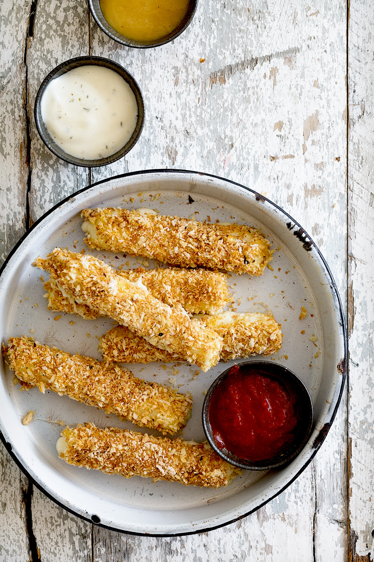 Six mozzarella sticks on a plate with a dipping bowl of marinara and additional bowls of ranch and honey mustard on the table above the plate. 