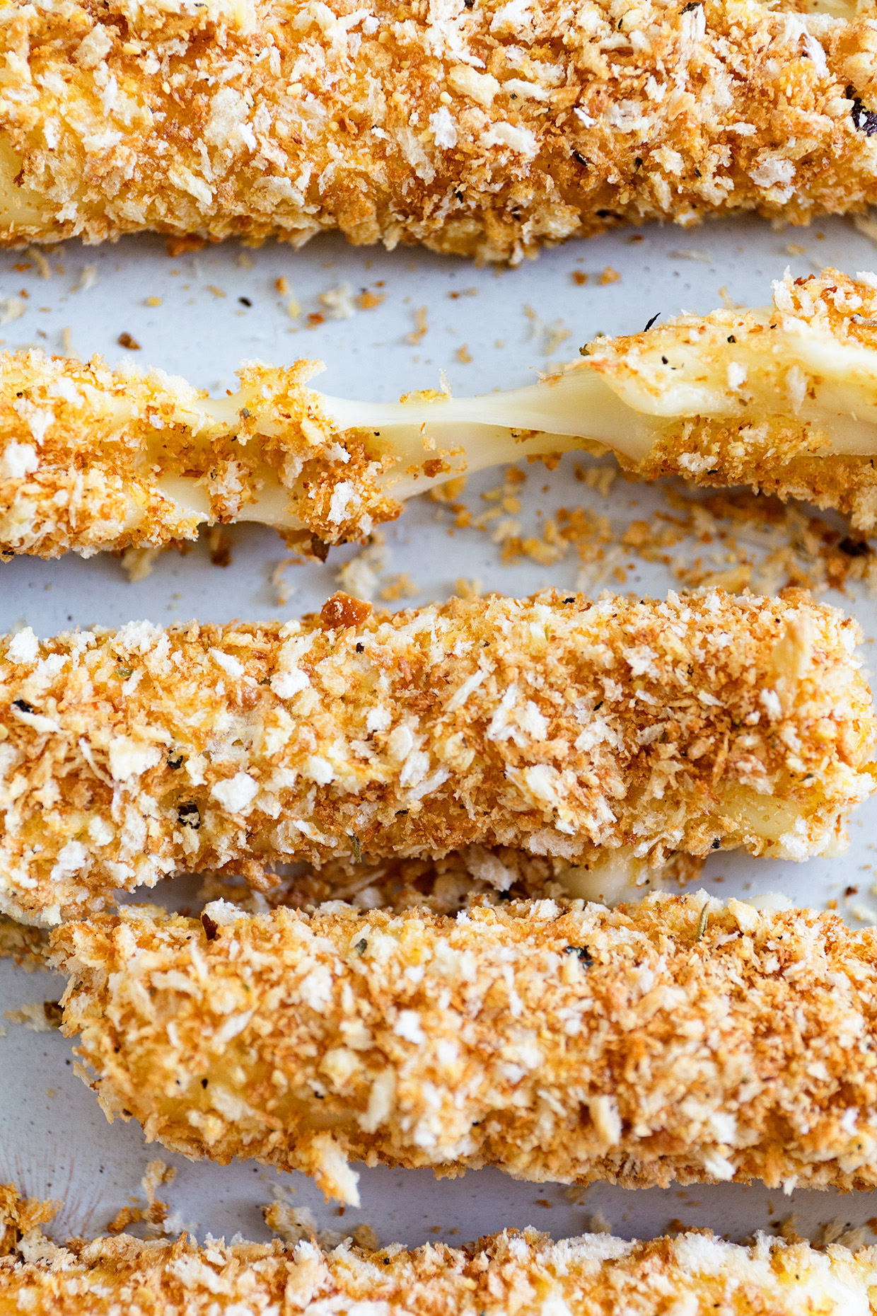 Close up of baked mozzarella sticks with one being pulled apart to see the cheese.