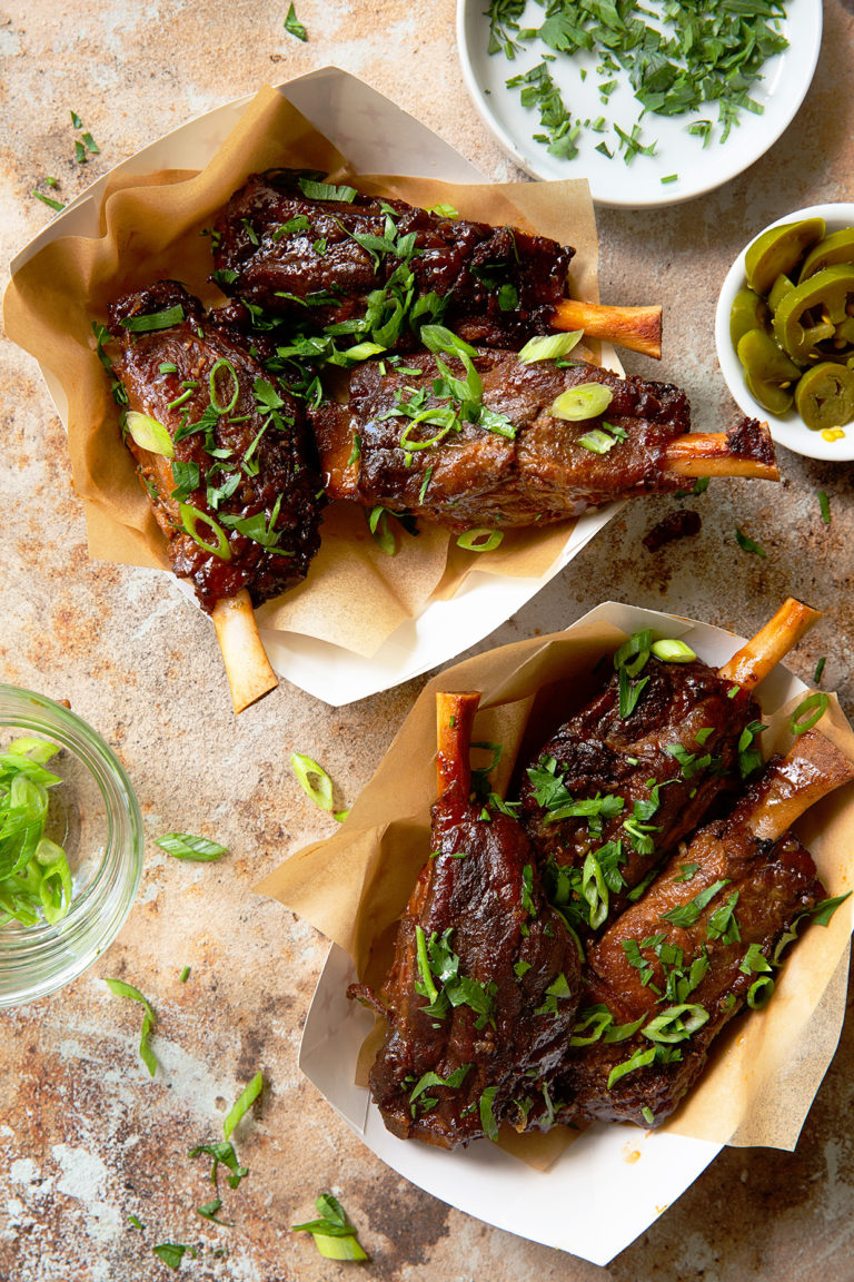 Two paper dishes full of three pig wings each surrounded by dishes of jalapeno, dip, and scallions.