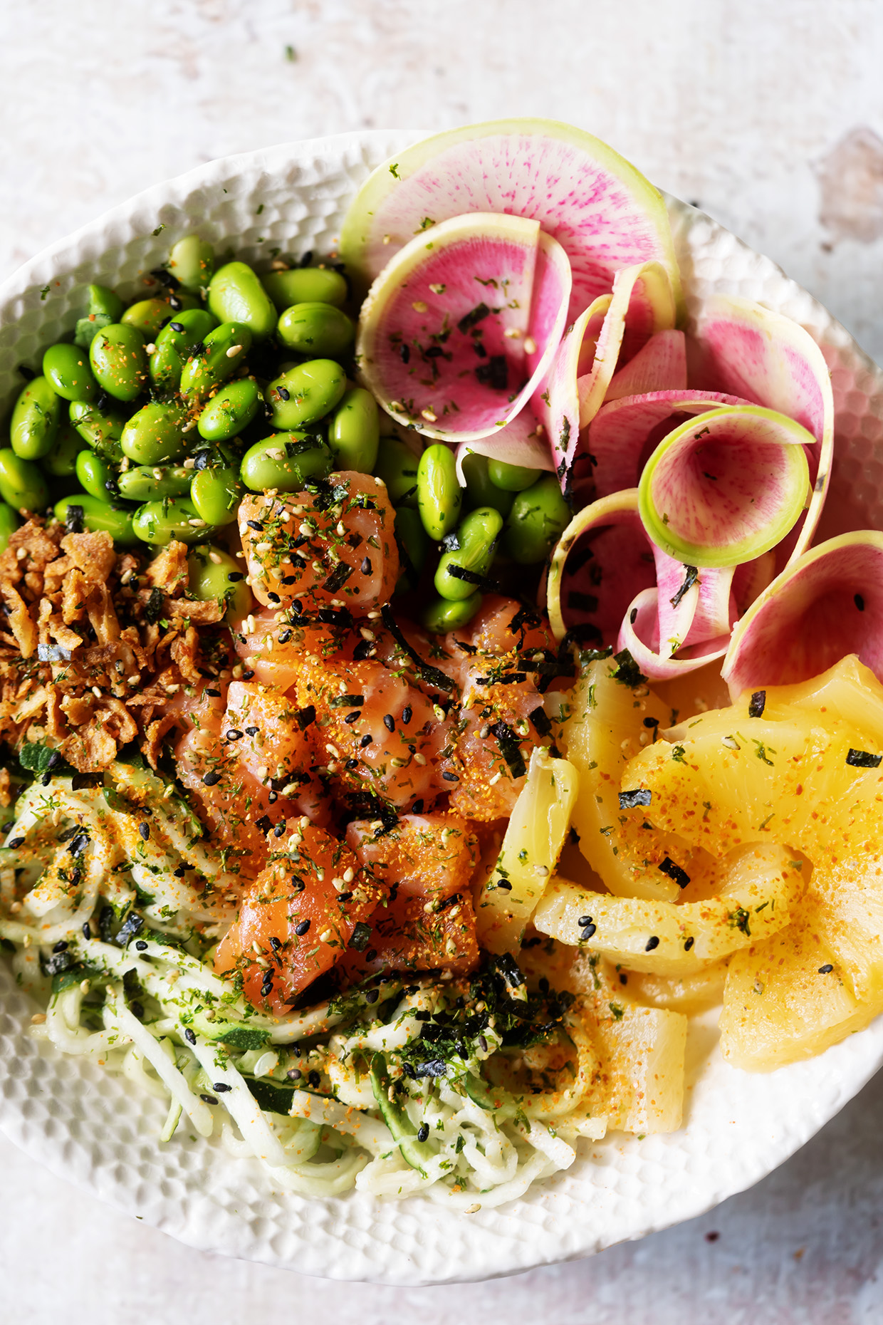 Salmon Poke Bowl with salmon, pineapple rings, radishes, edamame, and zucchini noodles.
