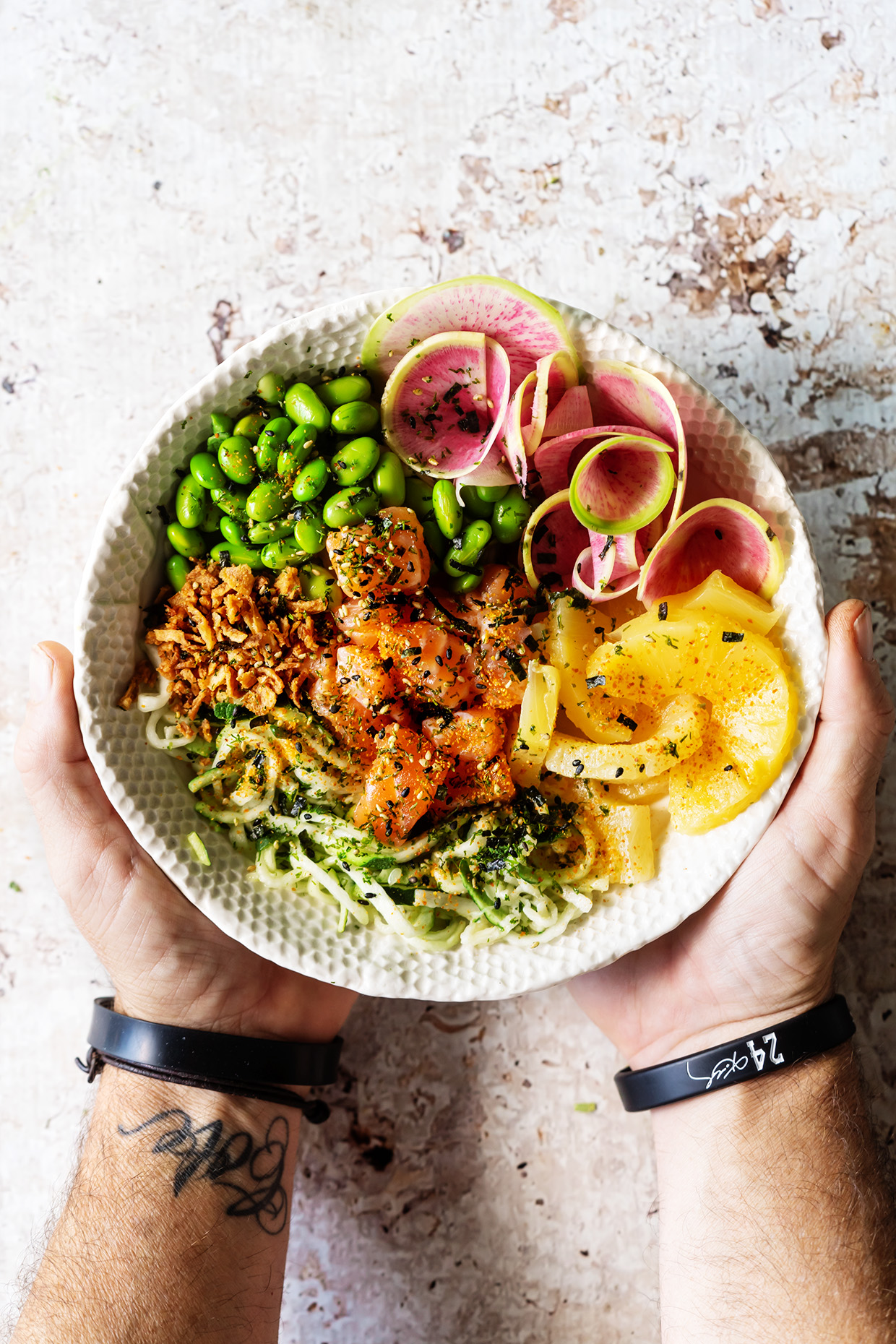 Salmon Poke Bowl with salmon, pineapple rings, radishes, edamame, and zucchini noodles.