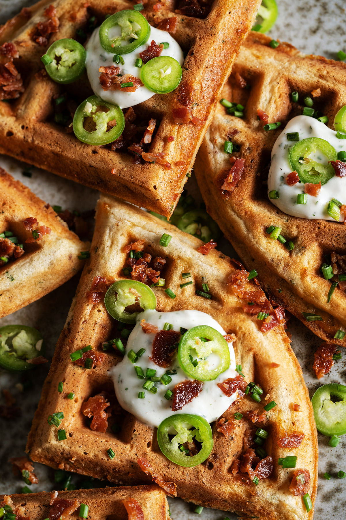Crispy bacon cheddar savory waffles topped with sour cream, jalapeño slices, chives, and crumbled bacon.